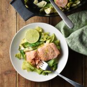 Salmon with chopped cabbage and fork in white bowl, with green cloth and black dish with salmon in background.