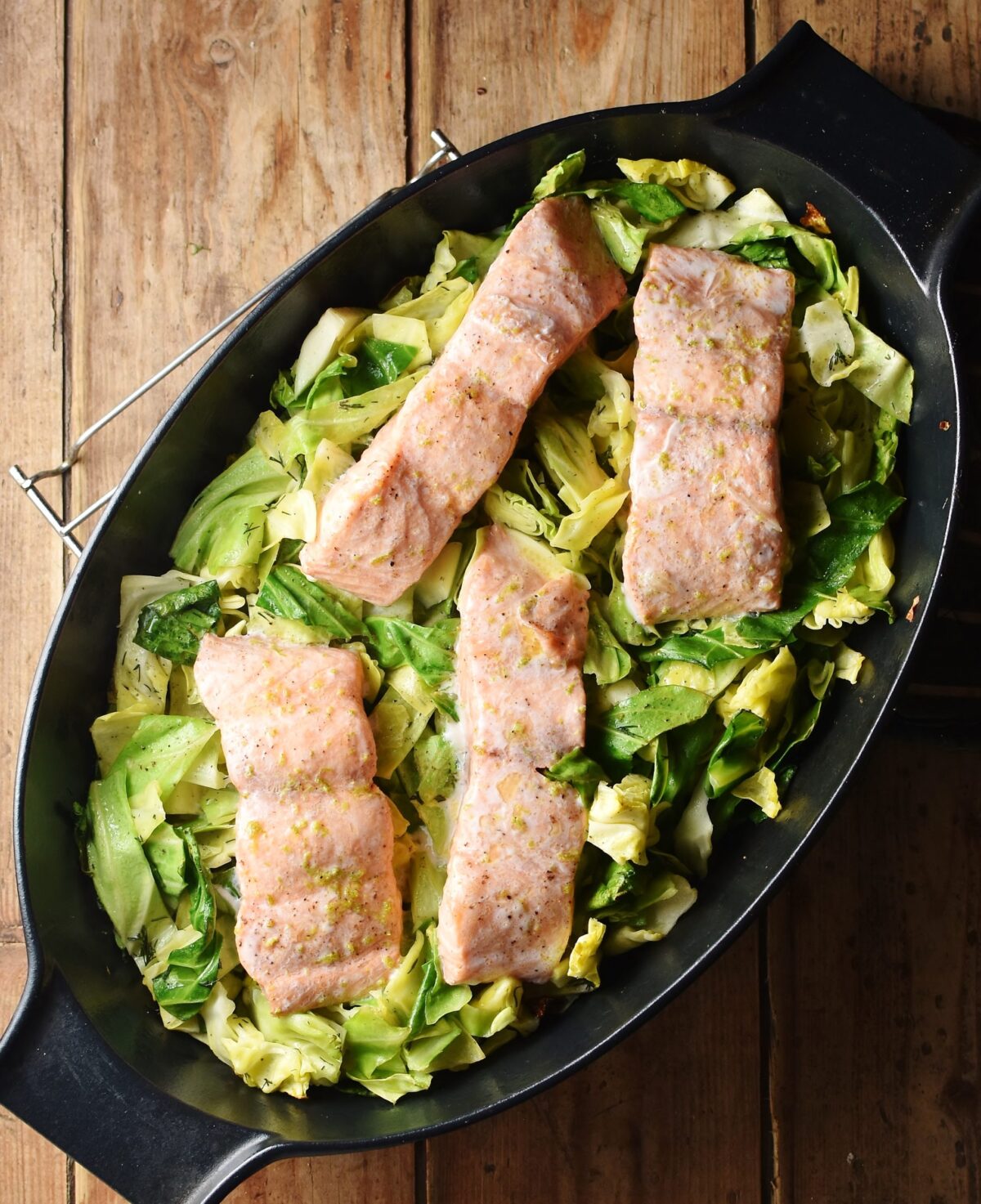 4 salmon pieces on a bed of cabbage in black oval dish.