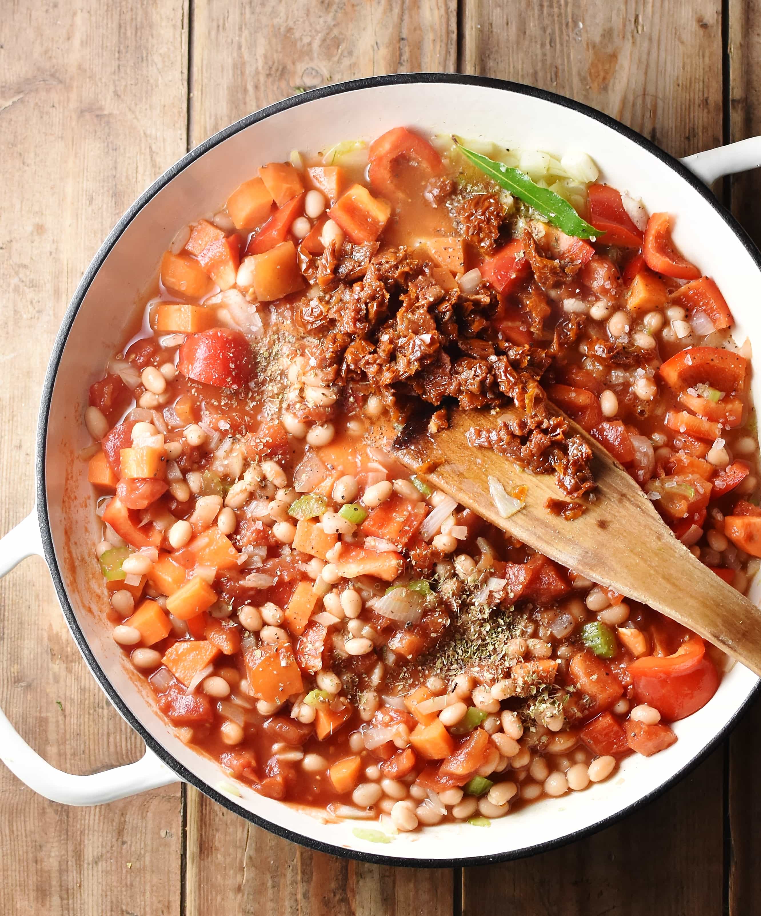 Vegetable mixture in large white shallow dish with wooden spoon.
