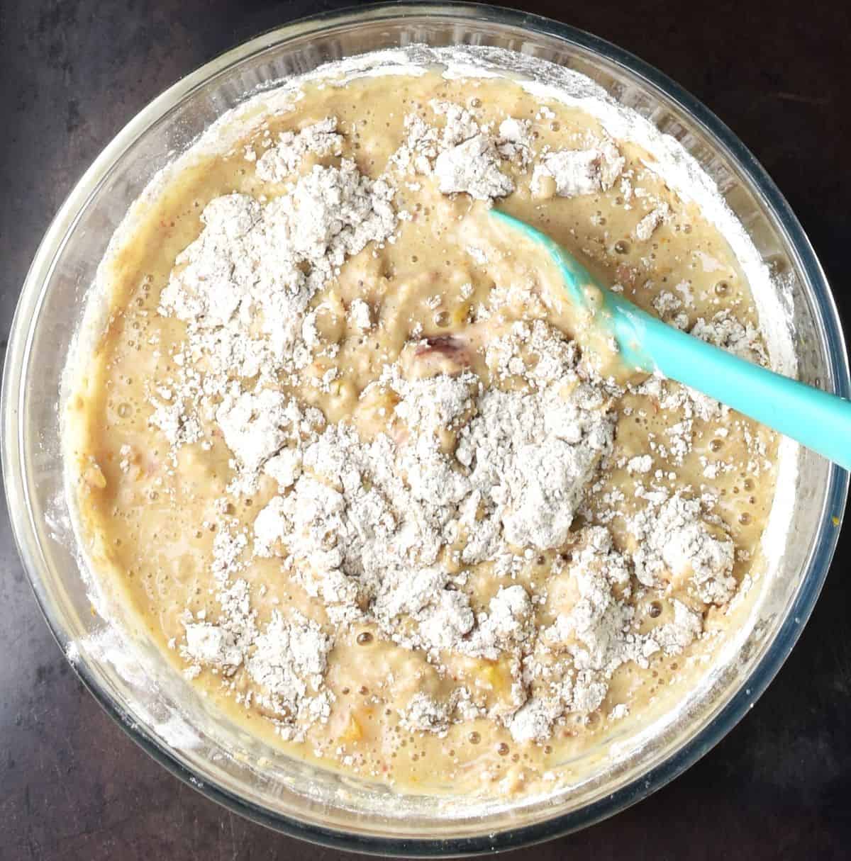 Blood oranges muffin batter with blue spatula in glass bowl.
