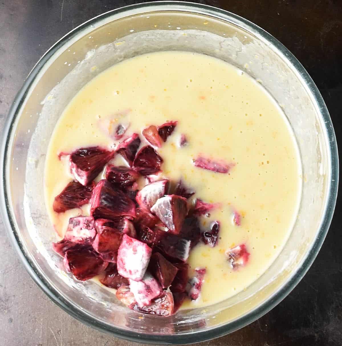 Chopped blood oranges in muffin batter in glass bowl.
