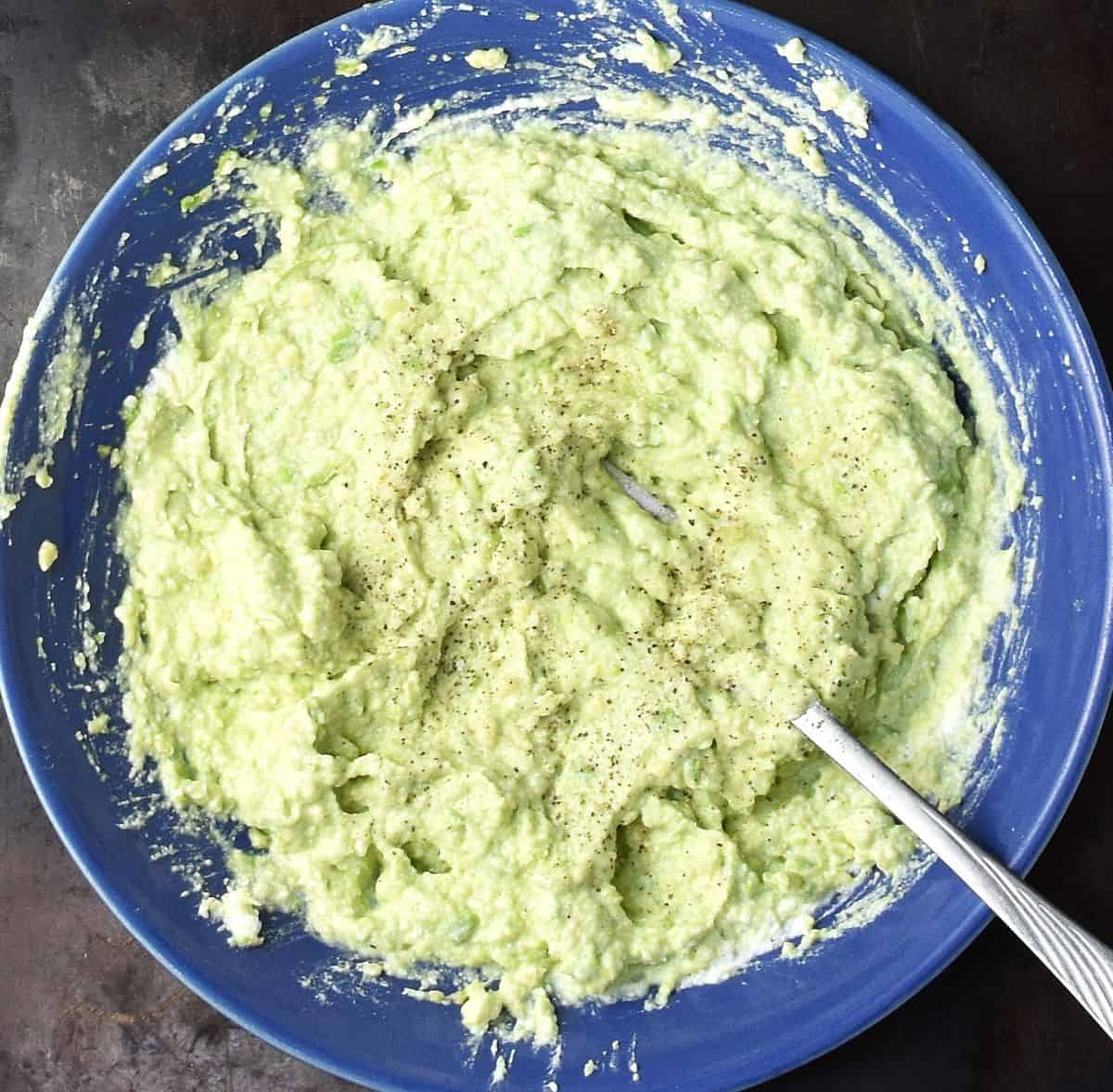 Top down view of mashed avocado and ricotta with fork in blue bowl.
