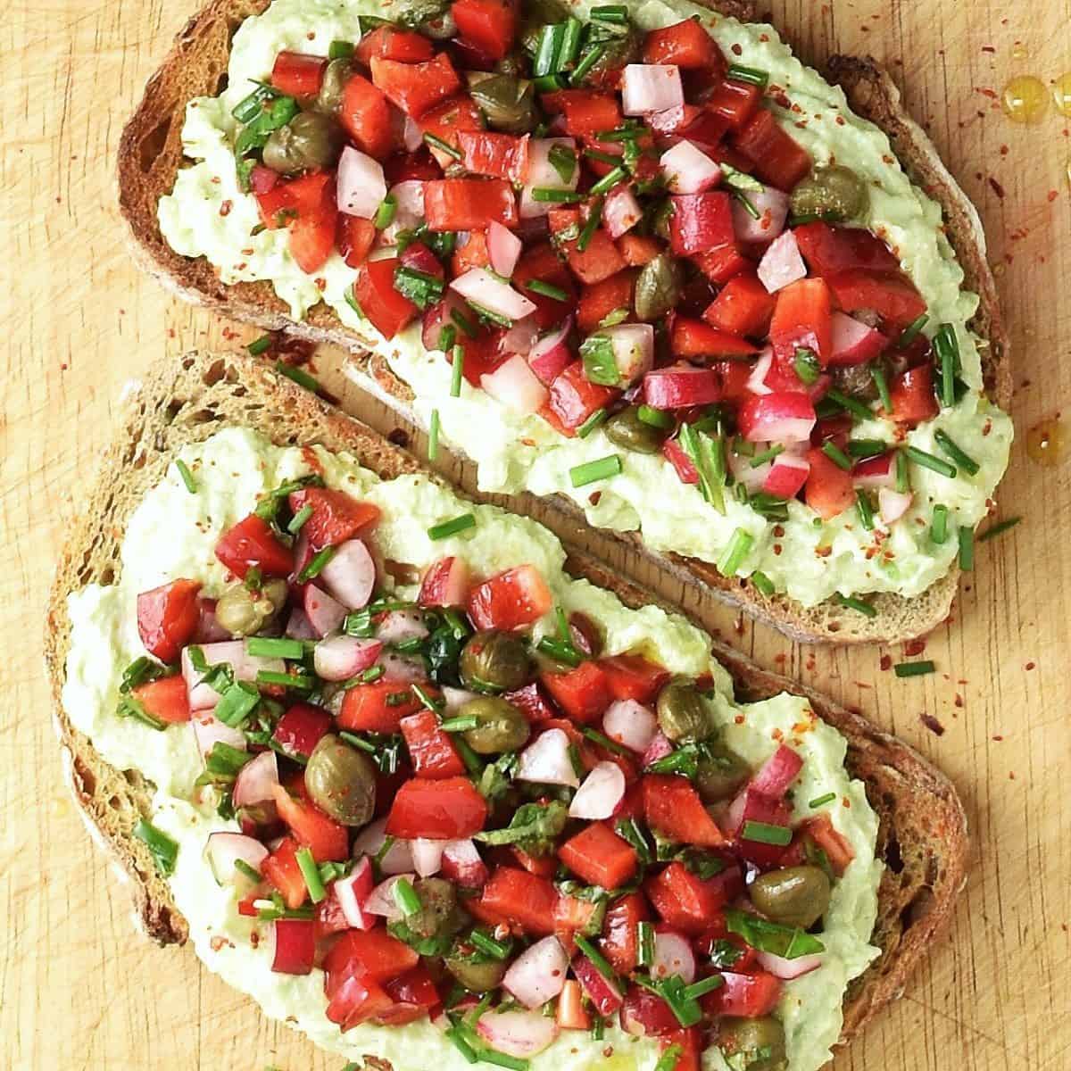 2 slices of bread topped with avocado ricotta mixture and chopped vegetables.