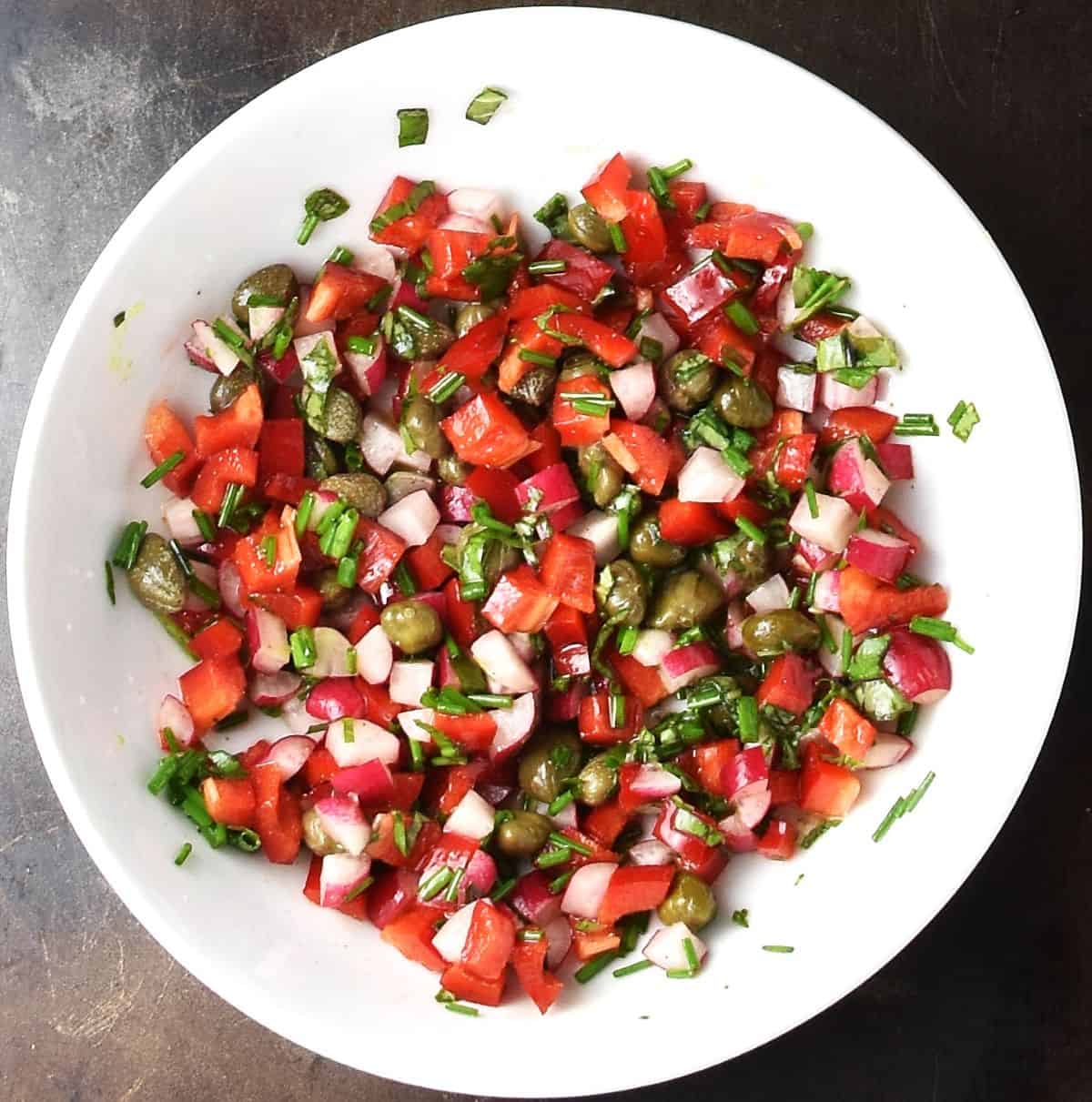 Top down view of finely chopped vegetables and herbs in white bowl.