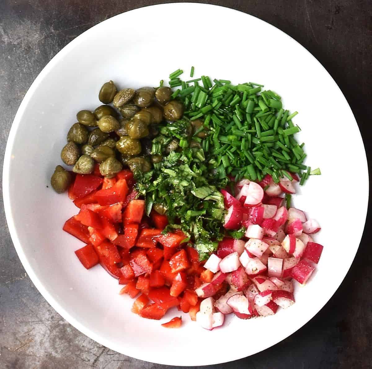 Chopped vegetables and herbs in white bowl.