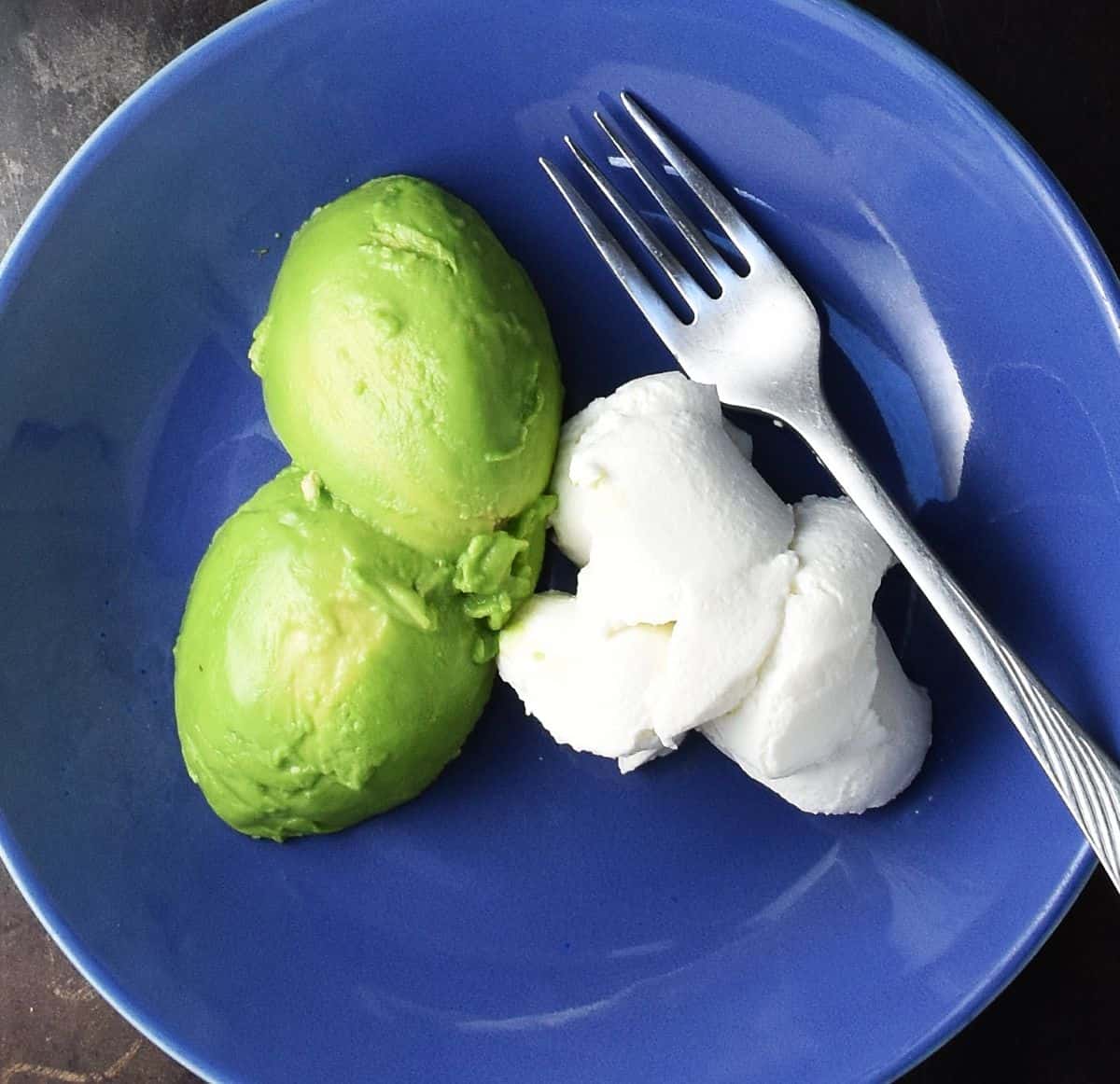 Peeled avocado and ricotta cheese in blue bowl with fork.