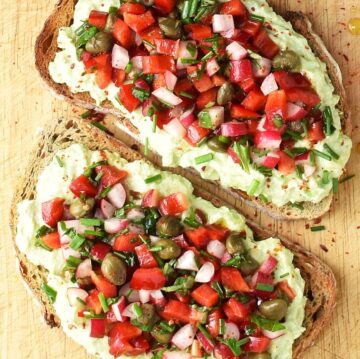 Top down view of 2 avocado ricotta toasts with chopped vegetables.