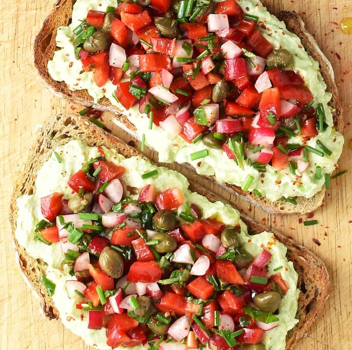 Top down view of 2 avocado ricotta toasts with chopped vegetables.