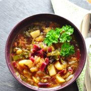 Beet greens vegetable soup in purple bowl with green cloth and spoon.