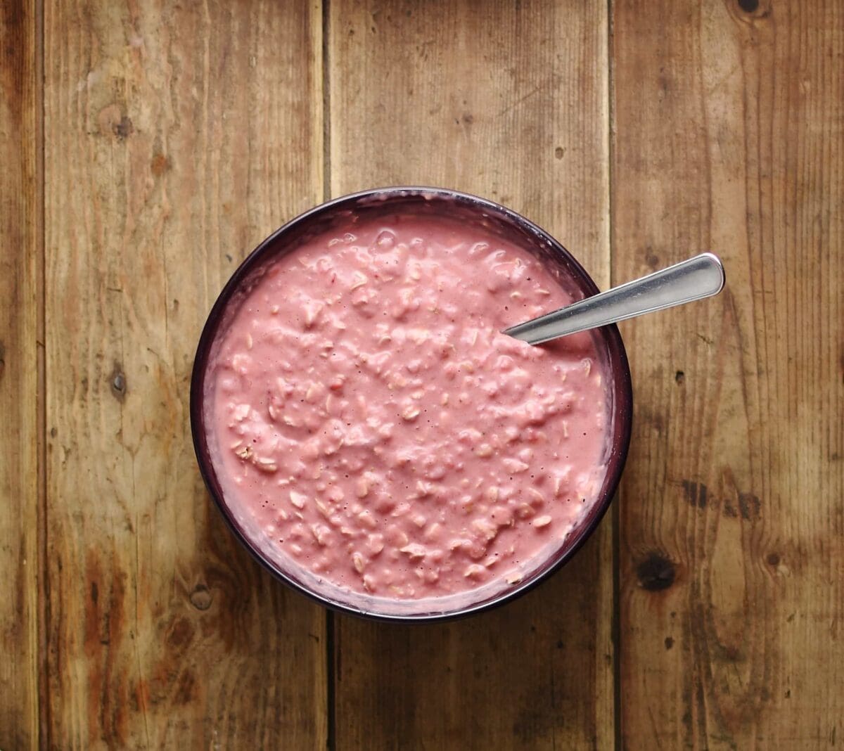 Top down view of strawberry overnight oats with spoon in purple bowl.
