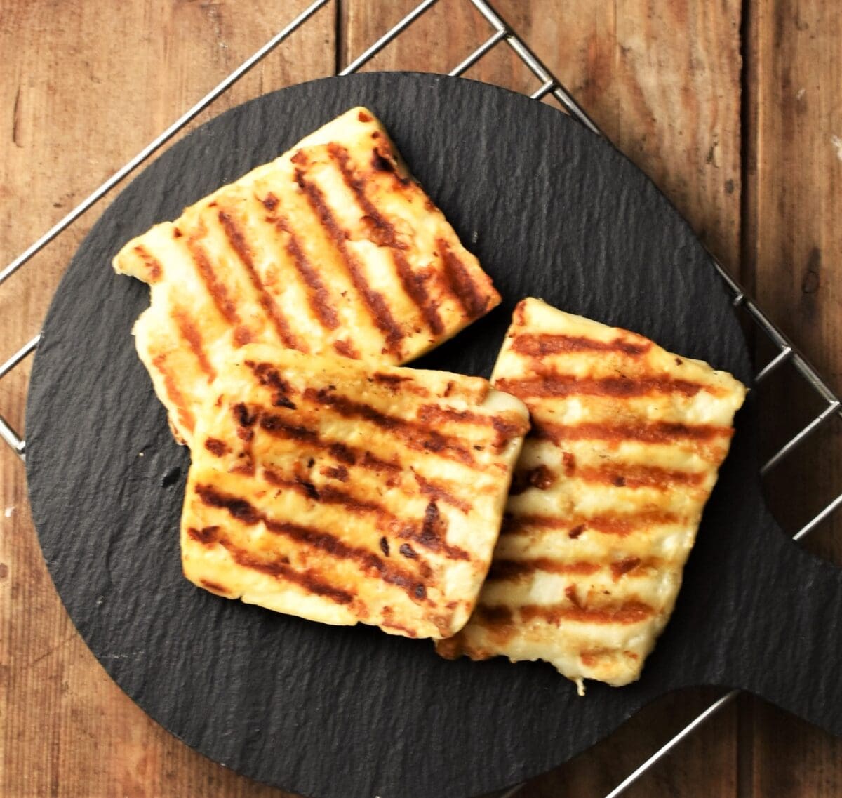 3 slices of grilled halloumi cheese on top of black platter.