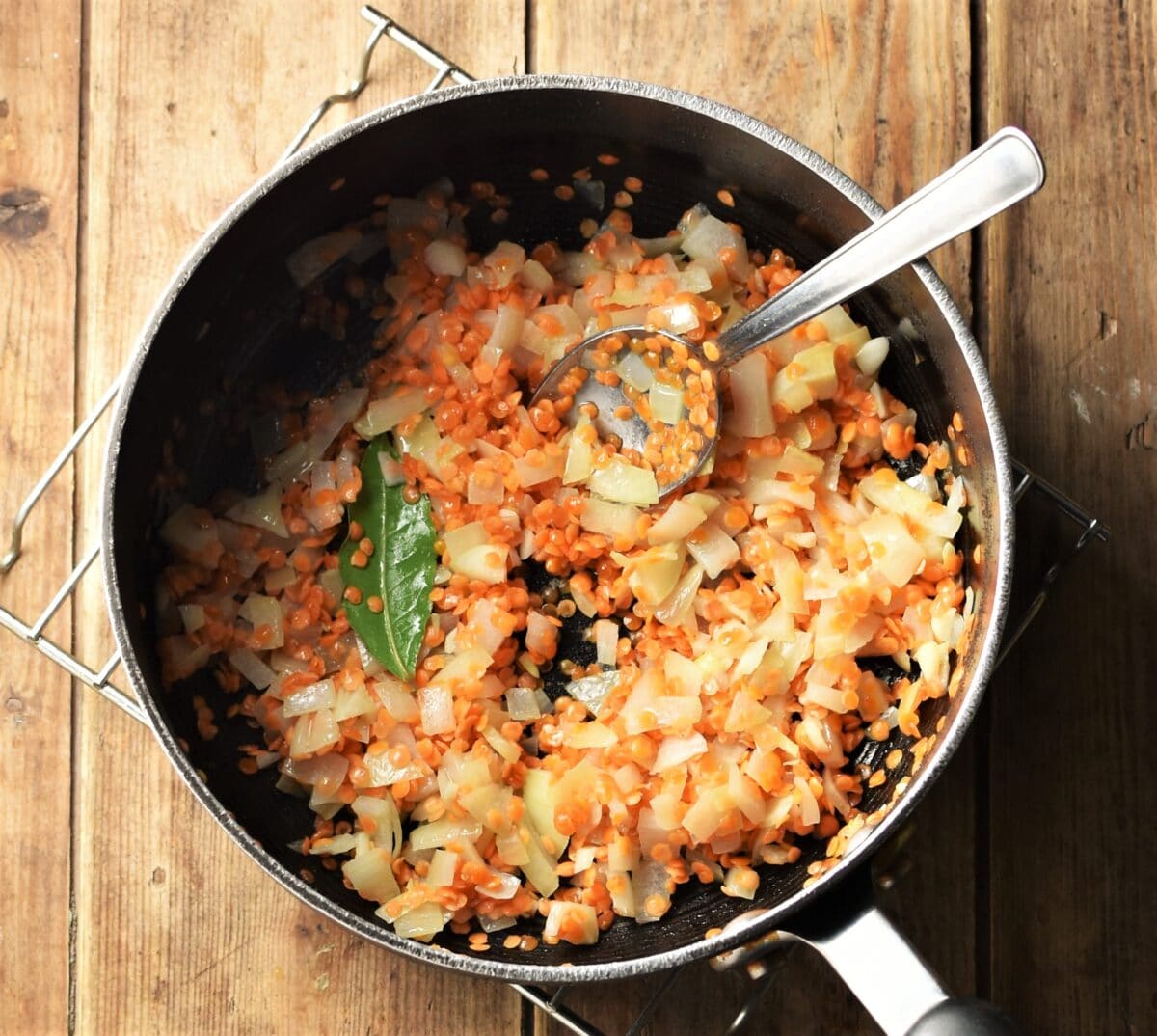 Red lentils, chopped onion and bay leaf in large pot with spoon.