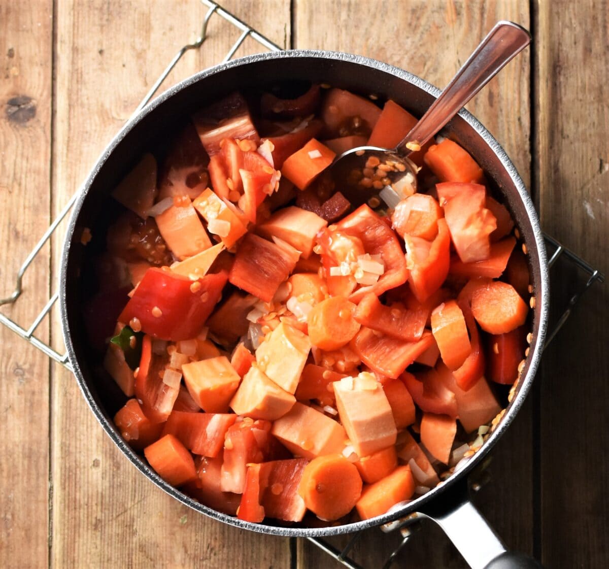 Chopped sweet potato, carrot and red pepper in large pot with spoon.