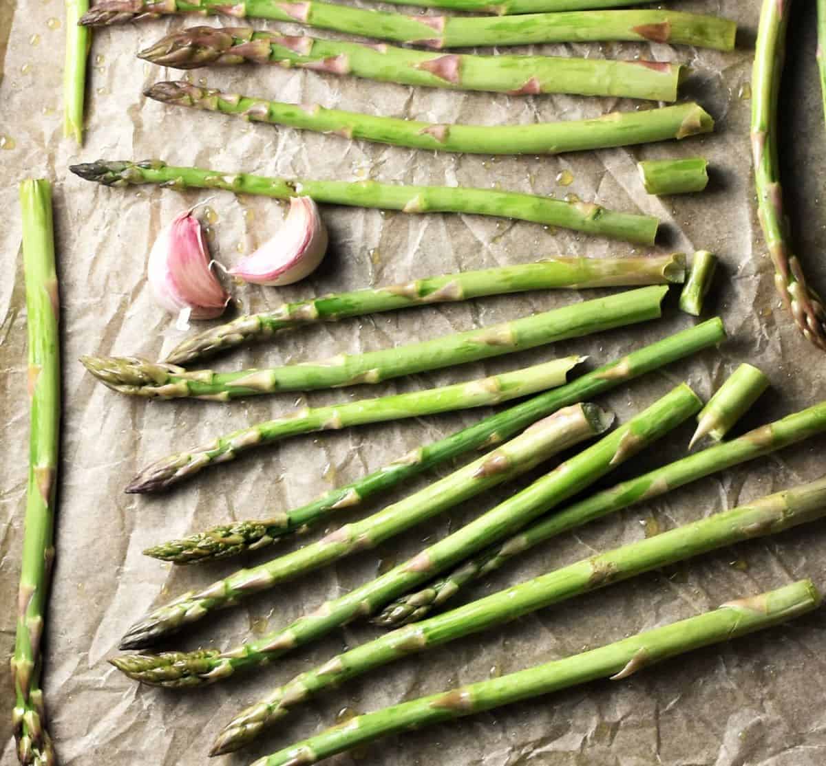 Asparagus spears and garlic cloves spread on parchment.