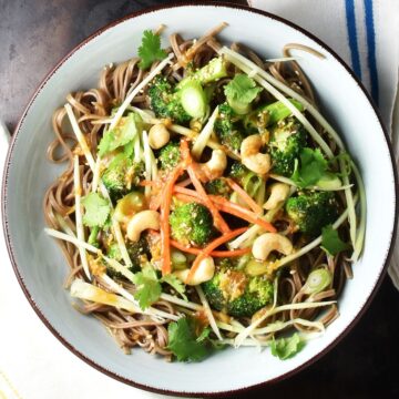 Top down view of broccoli noodle salad with shredded vegetables in blue bowl.