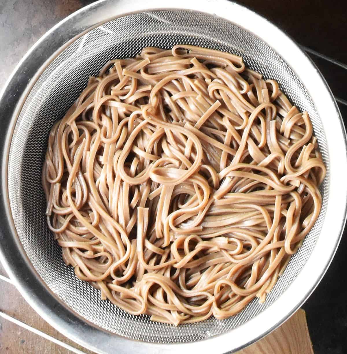 Cooked soba noodles in metal strainer.