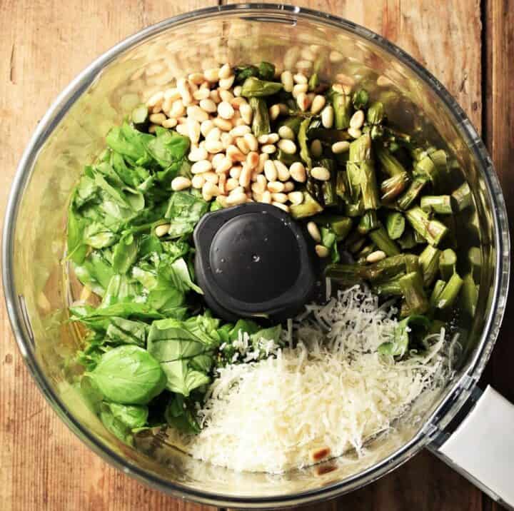 Top down view of asparagus and other pesto ingredients in food processor bowl.