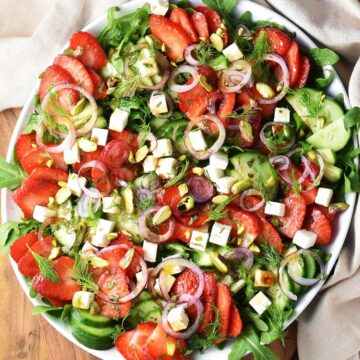 Top down view of strawberry cucumber salad with cubed feta and red onion on large white plate.