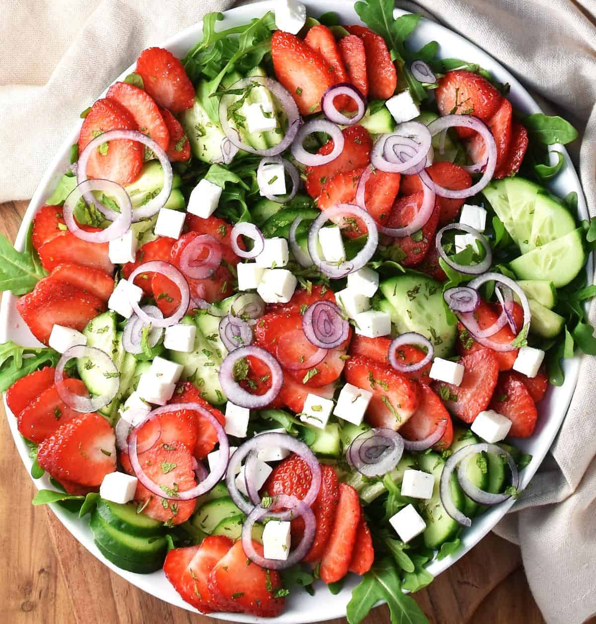 Strawberry cucumber salad with feta on top of wide white plate.