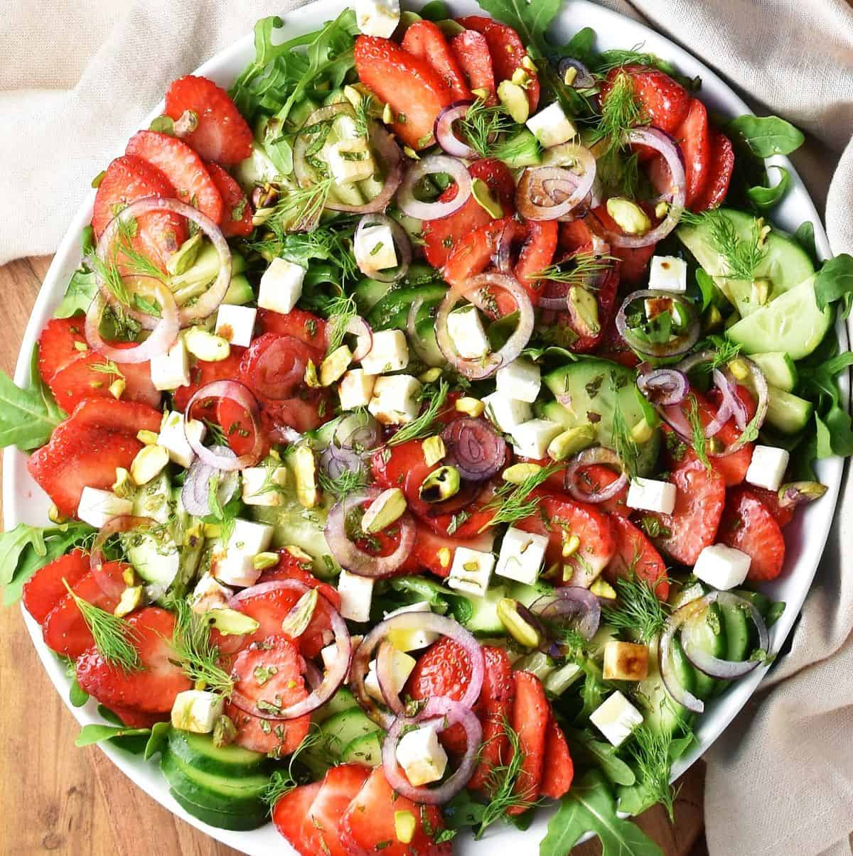 Top down view of strawberry cucumber salad with cubed feta and red onion on large white plate.