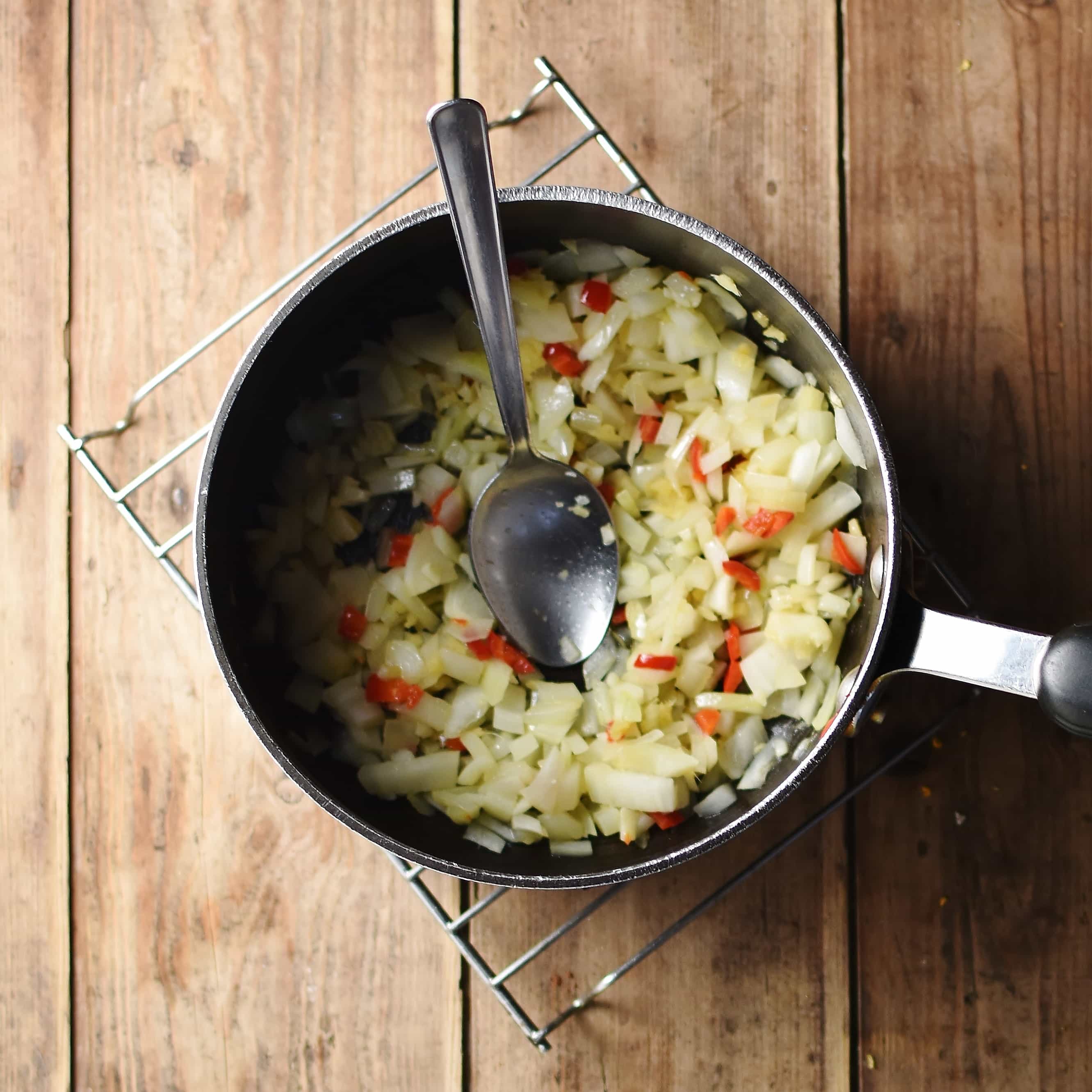 Fried onions and red chilli with spoon in large pot on top of cooling rack.