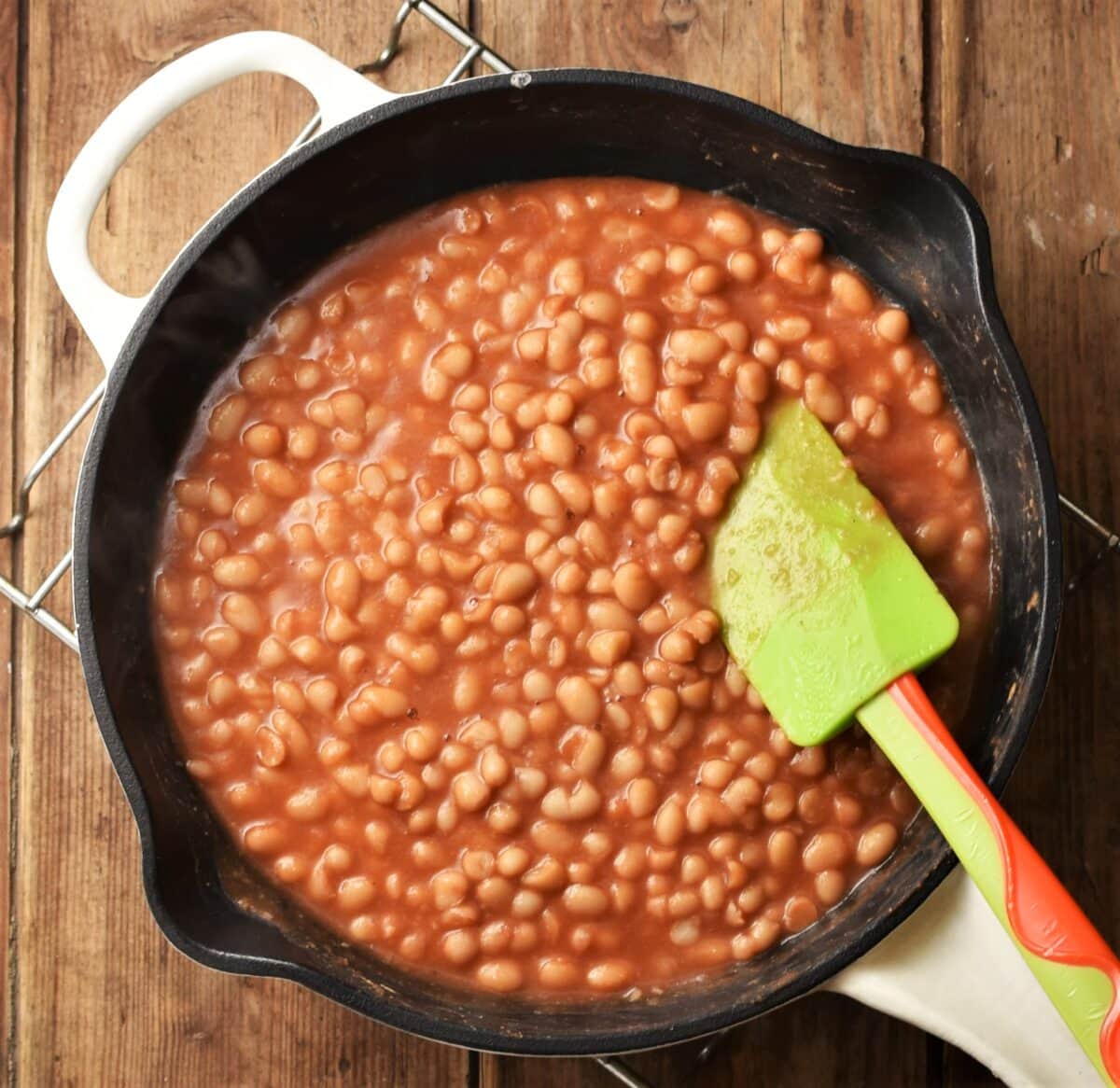 Top down view of beans in tomato sauce in skillet with green spatula.