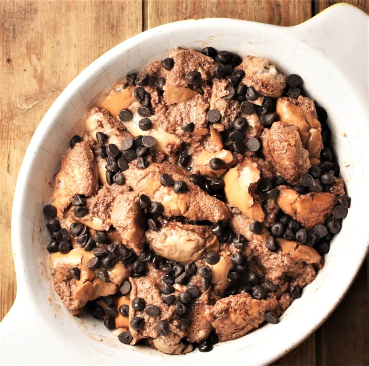 Making chocolate french toast casserole with chocolate chips in oval dish.