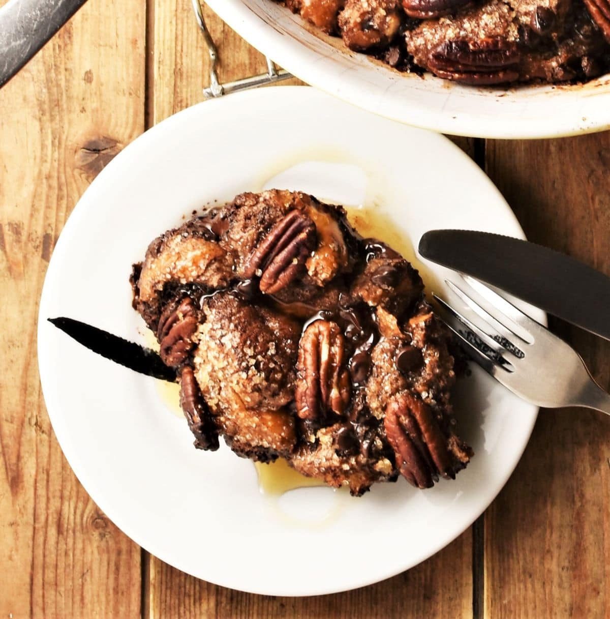Portion of chocolate french toast with pecans and maple syrup on white plate.
