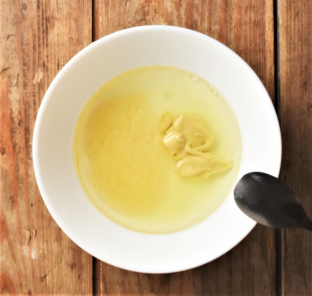 Salad dressing ingredients in white bowl with spoon.