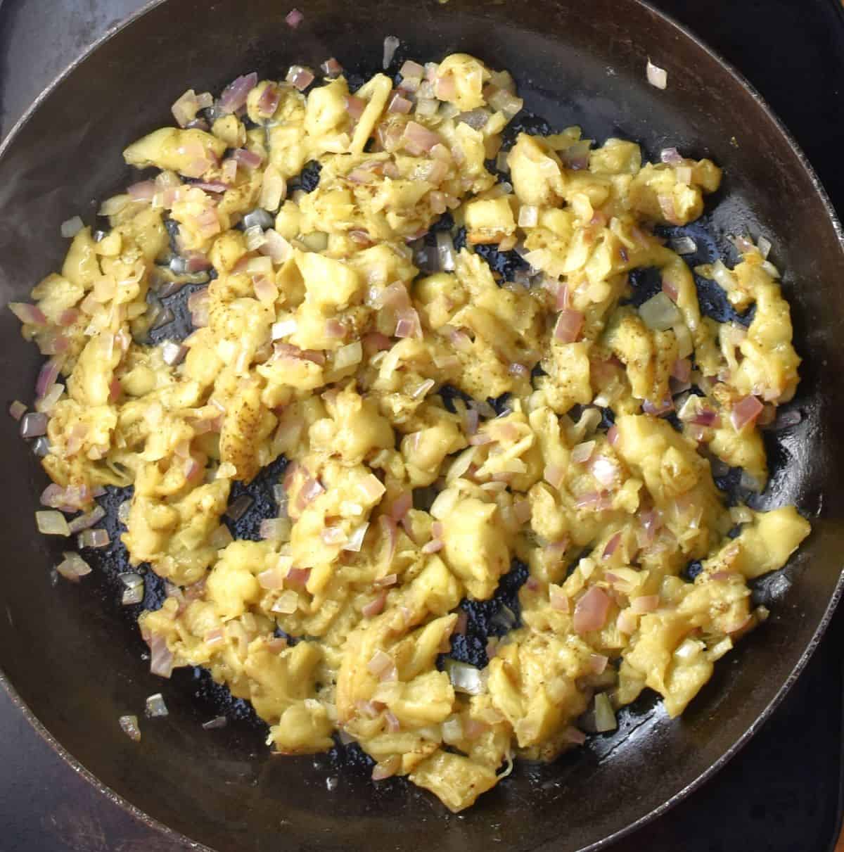 Cooking eggplant flesh with onion in large pan.
