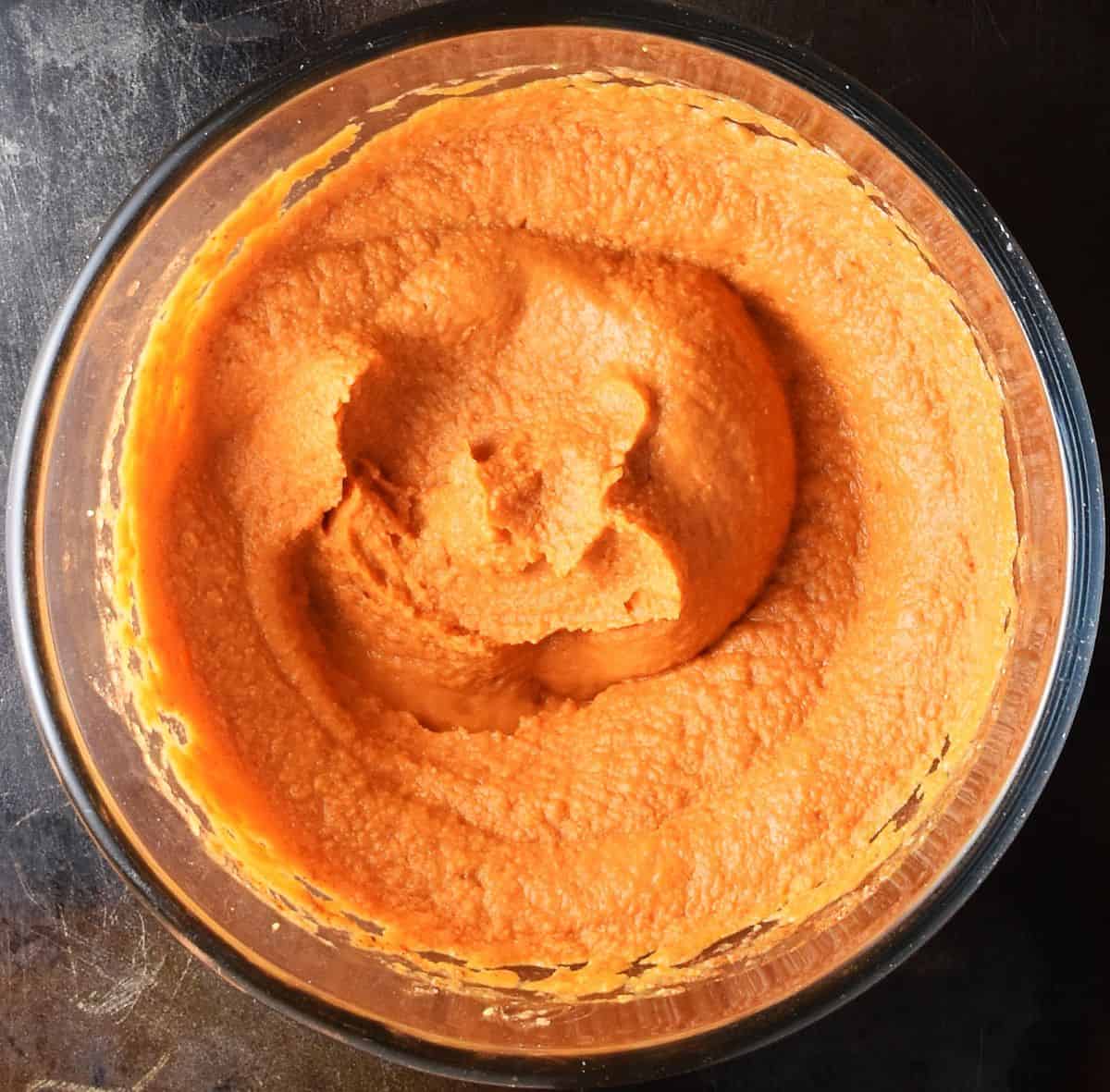 Top down view of creamy roasted red pepper hummus in glass bowl.