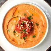 Top down view of roasted red pepper hummus without tahini garnished with peppers and seeds in white bowl.