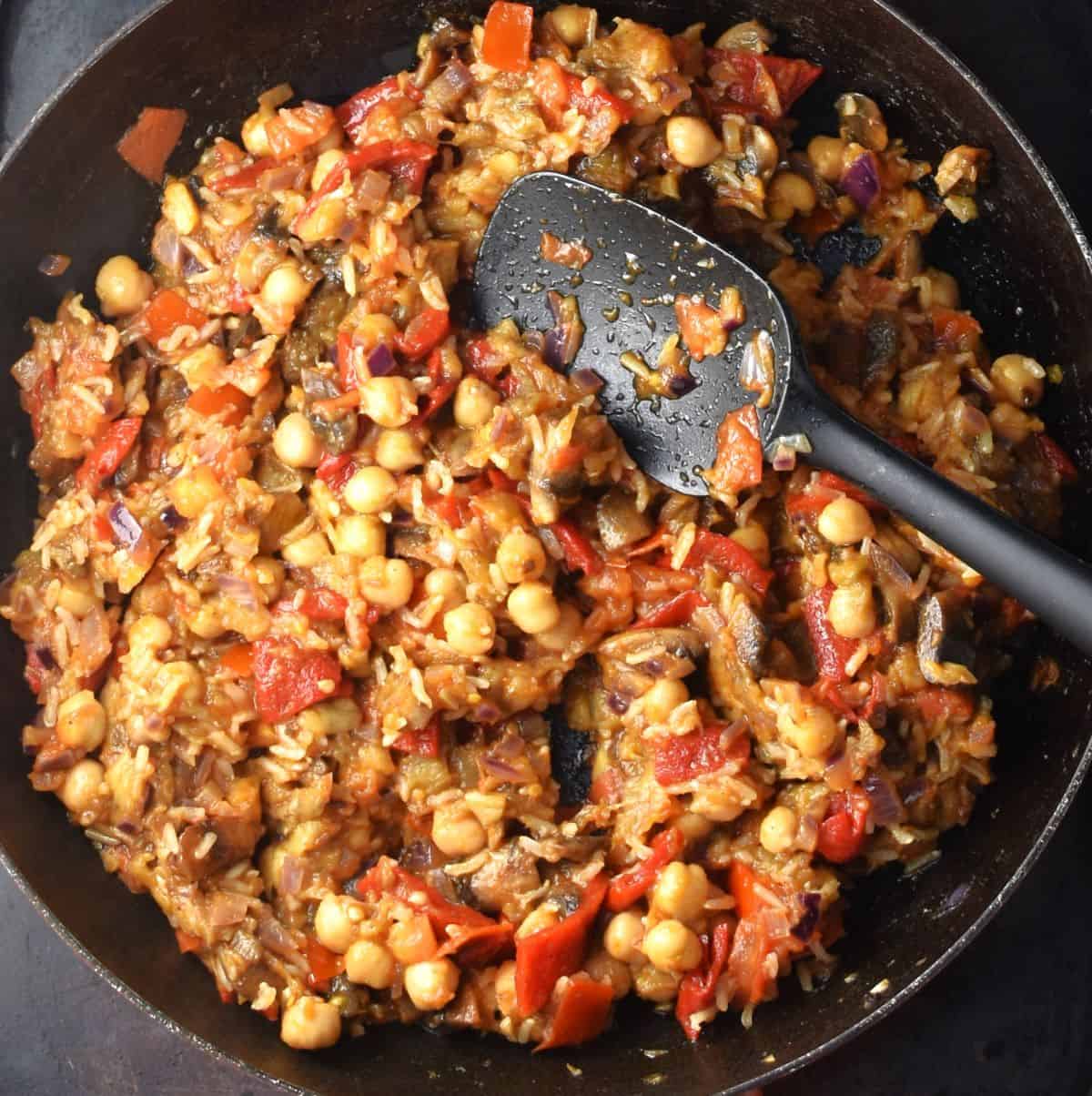 Eggplant stuffing mixture in large pan with black spoon.