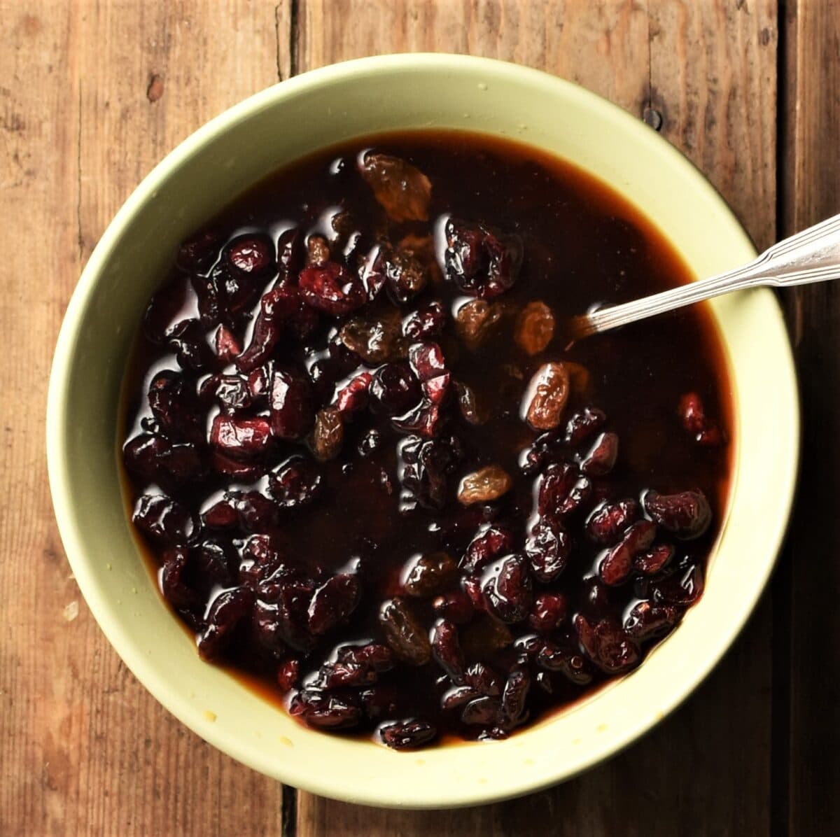 Cranberries in rooibos tea in yellow bowl with spoon.