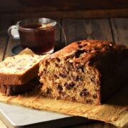 Side view of tea cake with slice on top of parchment, with cup of tea in background.