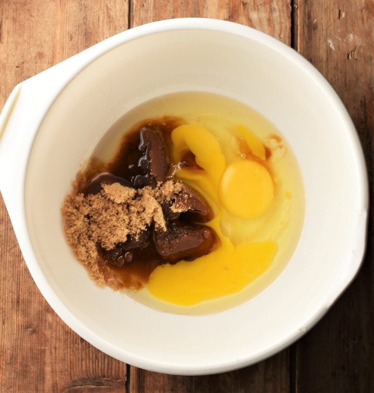 Eggs and brown sugar in white mixing bowl.