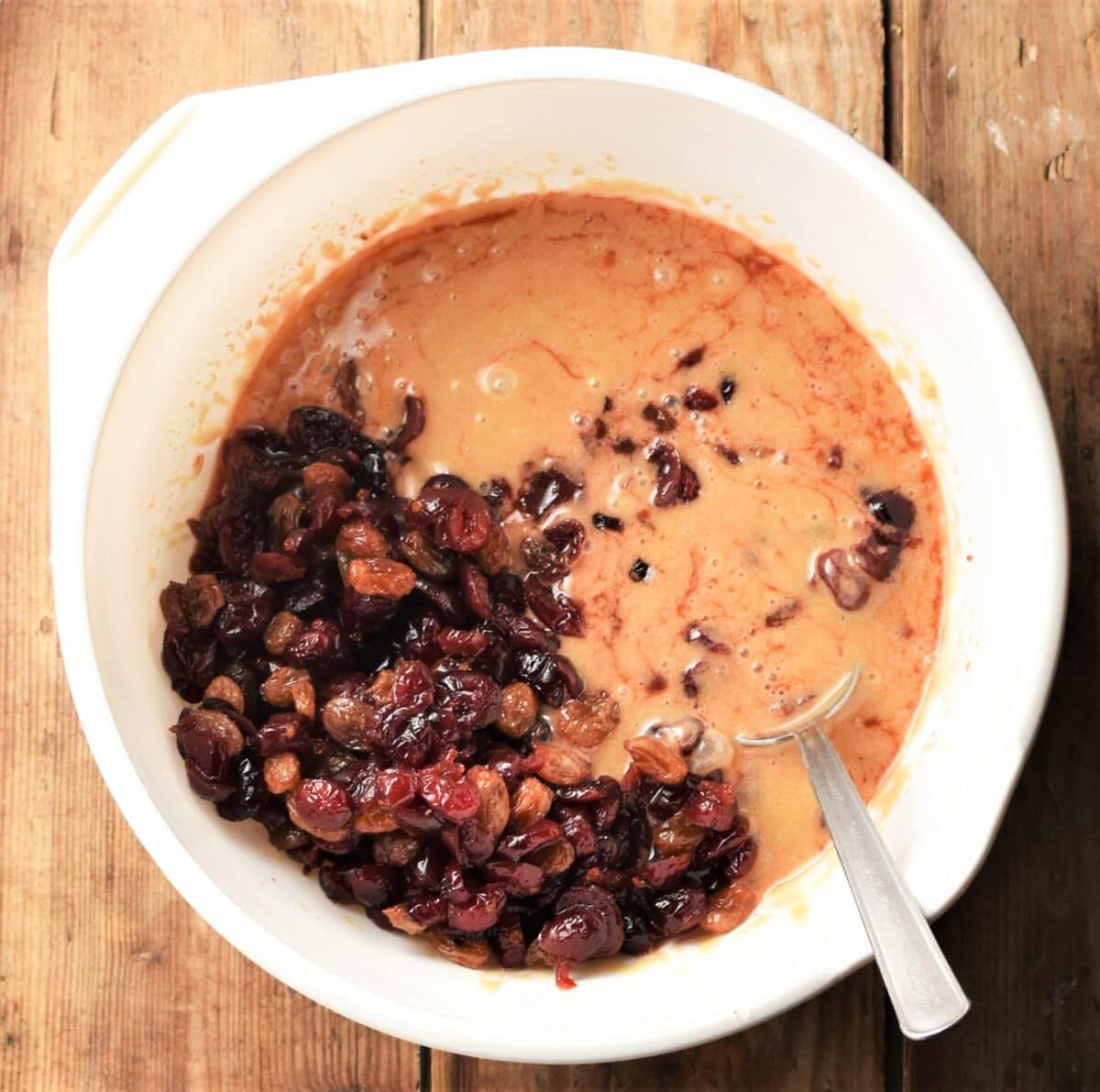 Cake batter with cranberries in white bowl with spoon.