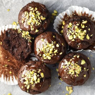 Top down view of 6 avocado chocolate muffins with chocolate glaze on parchment.
