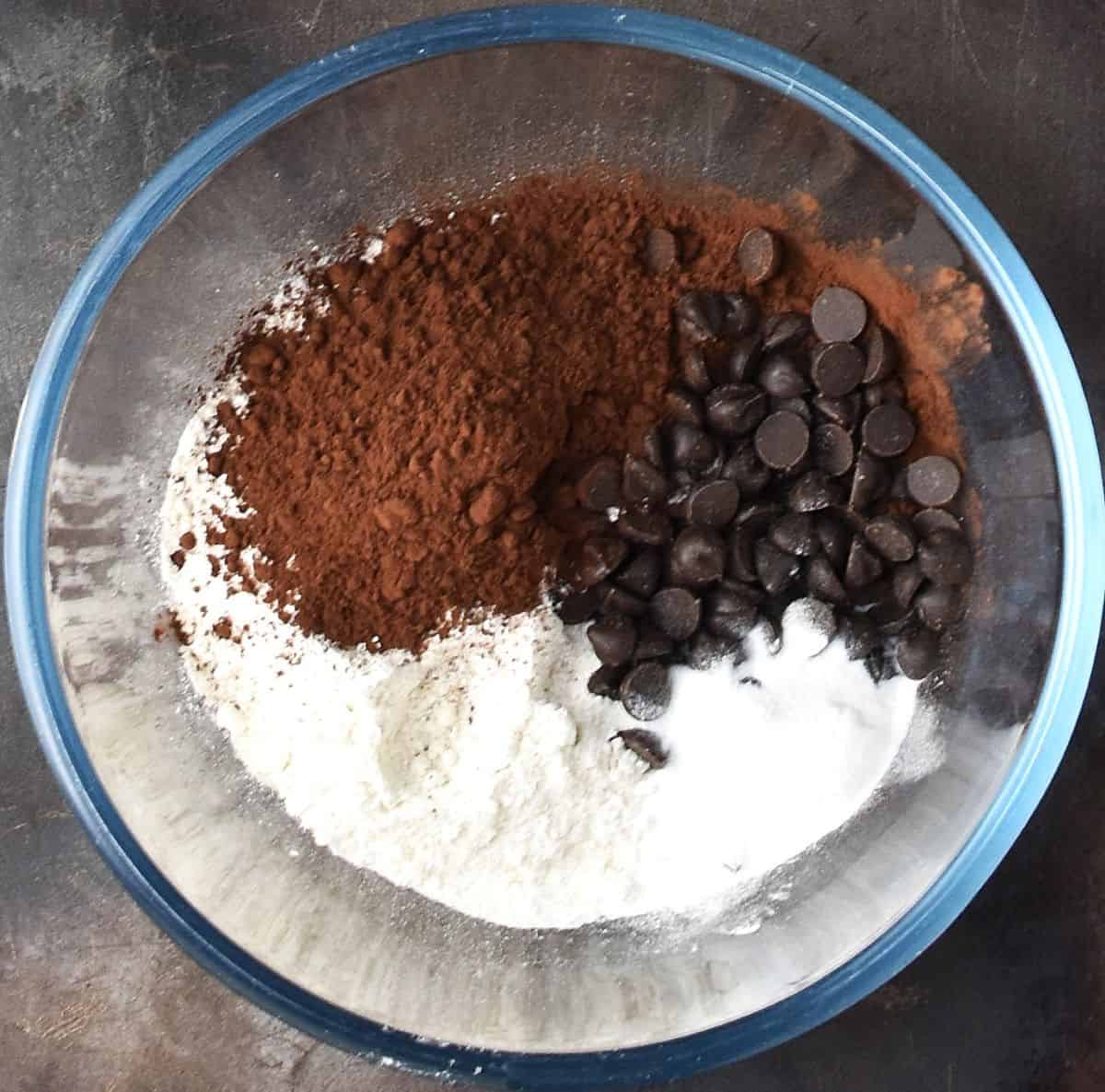 Flour, cocoa powder and chocolate chips in glass bowl.