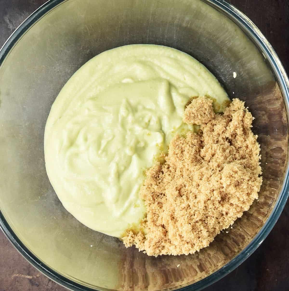 Top down view of creamy avocado mixture for muffins and brown sugar in glass bowl.