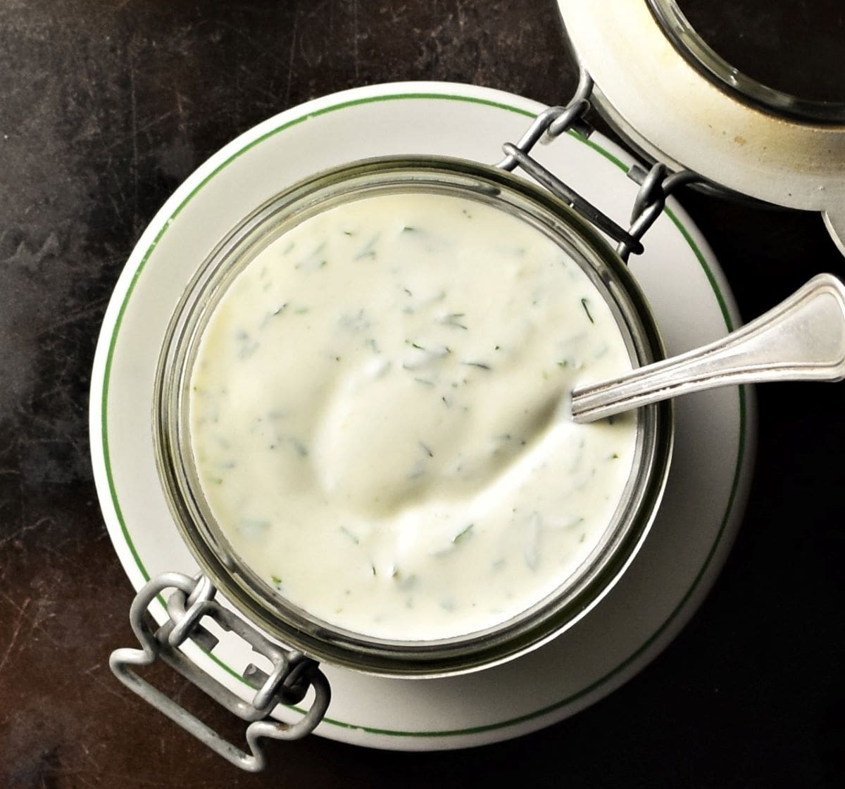 Top down view of ranch sauce in open jar with spoon on top of saucer.