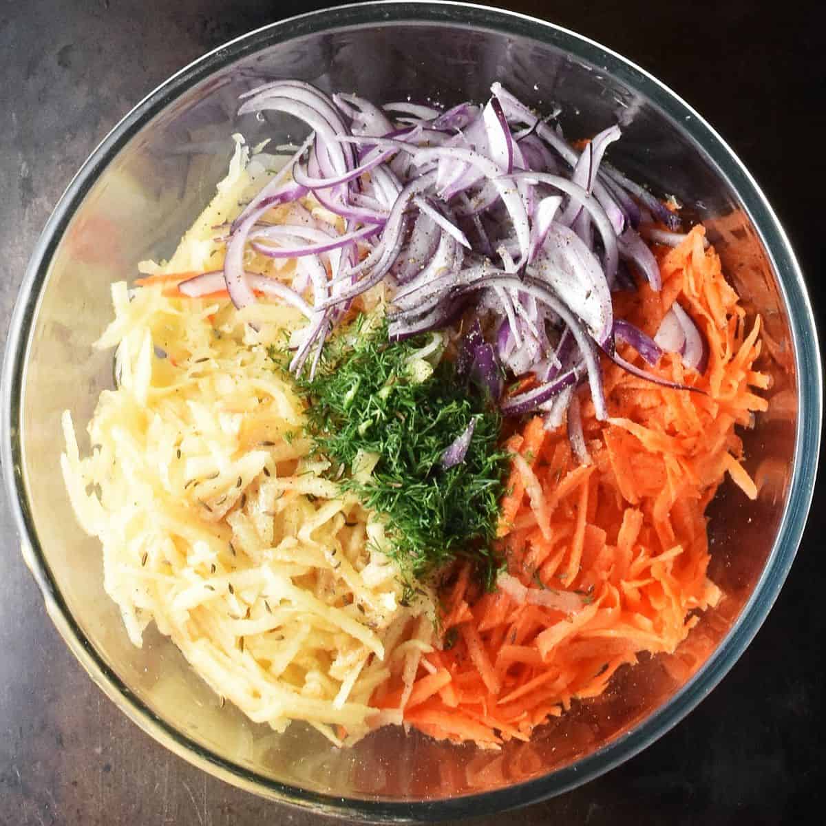 Sauerkraut with shredded vegetables and chopped herbs in glass bowl.