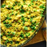 Top down view of curried chicken rice casserole in black oval cast iron dish on top of wooden board.
