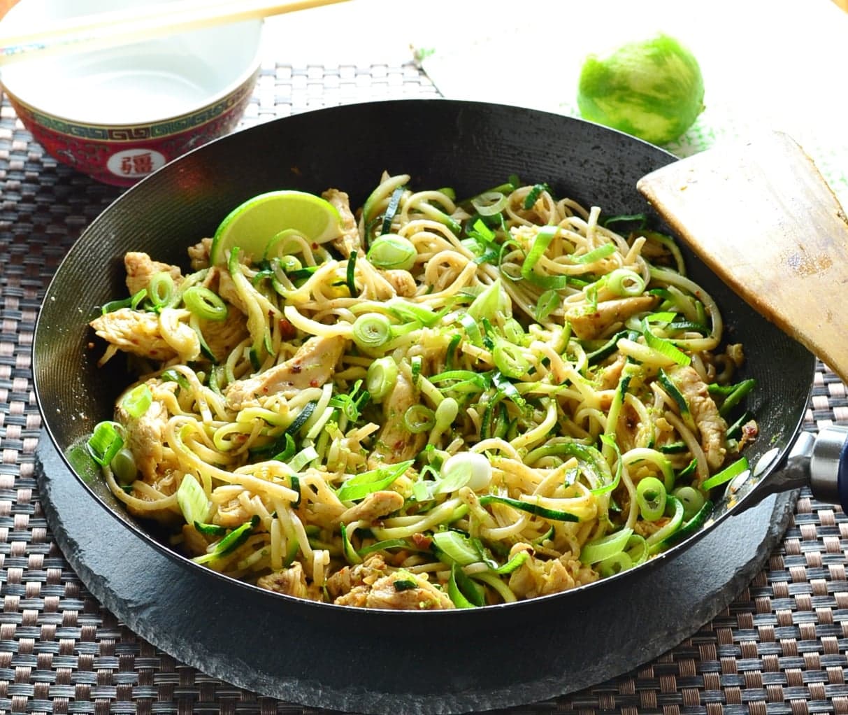Chicken stir fry in wok with lime in background.