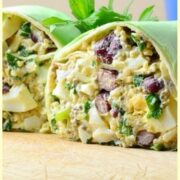 Side view of halved egg salad wrap on top of wooden board with parsley leaves in background.
