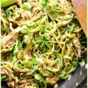Hoisin chicken stir fry in wok on slate round plate with lime, bowl with chopsticks and green cloth in background.