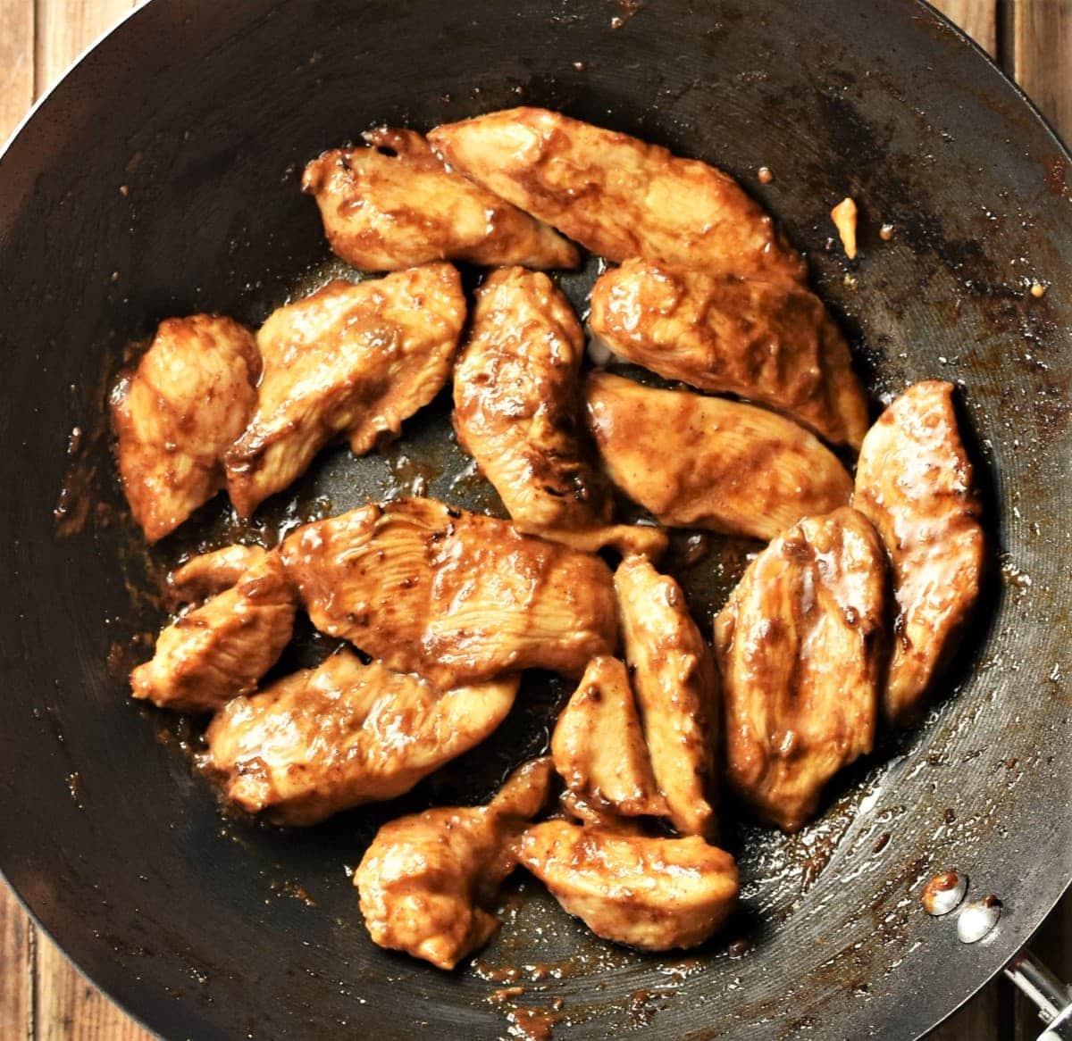 Stir fried marinated chicken strips in wok.