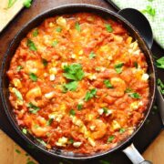 Tomato shrimp saganaki in large black pan on oven tray with spoon and green cloth.