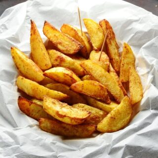 Spiced crispy potato wedges with cocktail sticks in basket lined with white paper.