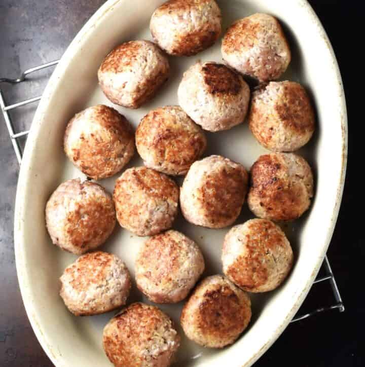 Browned meatballs in white oval dish.